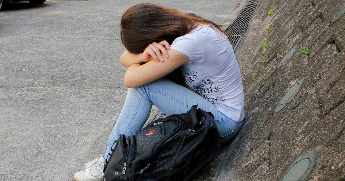 Imagem de uma jovem sentada com a cabeça entre as mãos, denotando profundo sofrimento