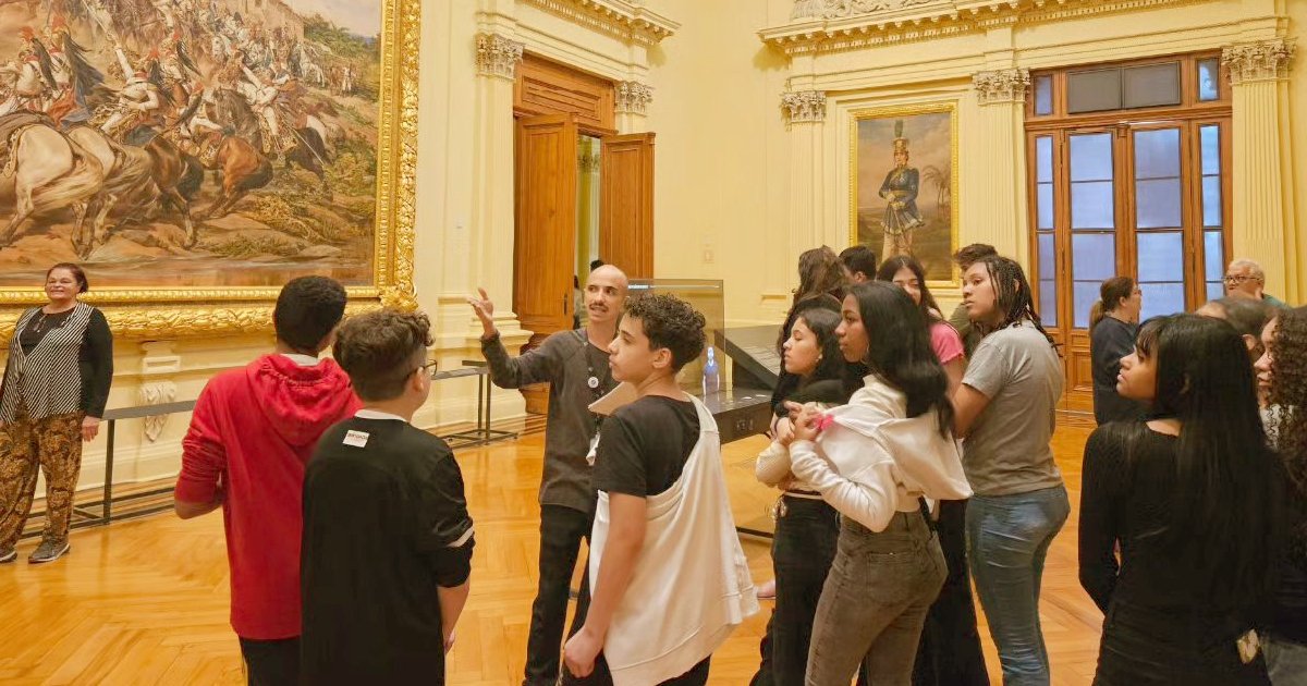 Grupo de pessoas num museu olhando para um quadro e uma pessoa apontando